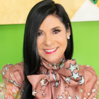 Smiling woman with long black hair wearing a pink star-pattern blouse against a green background.